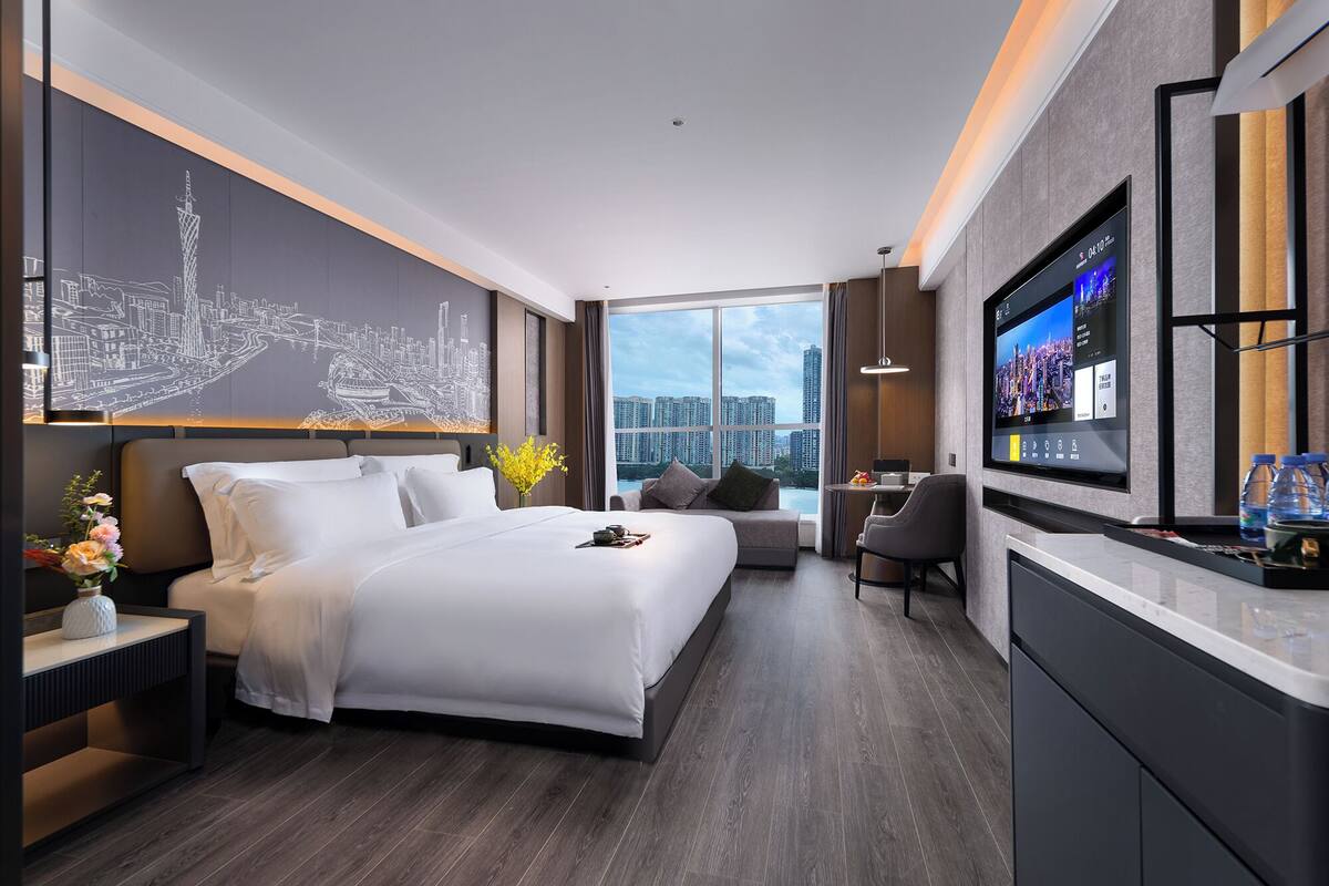 Una habitación de hotel moderna con una cama grande, un escritorio, un televisor y vistas a la ciudad.