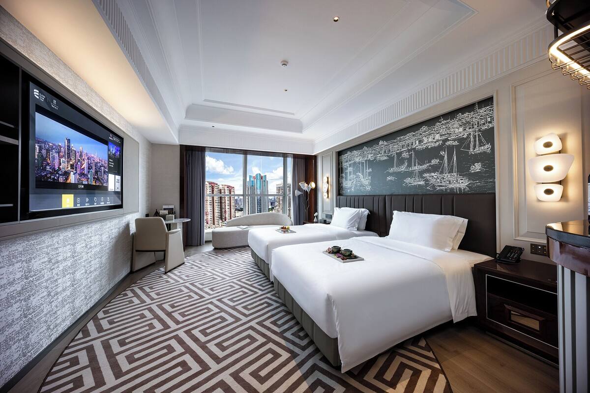 Habitación de hotel moderna con dos camas, un televisor grande, vistas a la ciudad y un adorno en la pared.