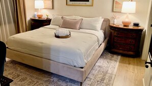 A neatly arranged hotel room with a large bed, two bedside tables with lamps, a framed artwork on the wall, and a patterned rug on the floor. - Cozy King Size 1-bedroom condo in adorable La Quinta with AC (La Quinta)