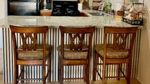A kitchen with wooden cabinets, a refrigerator, a microwave, a stove, and a bar area with three stools. - Cozy King Size 1-bedroom condo in adorable La Quinta with AC (La Quinta)