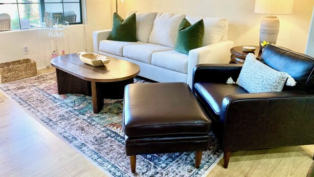 A living room with a white sofa, a black leather sofa, a coffee table, and a patterned rug. - Cozy King Size 1-bedroom condo in adorable La Quinta with AC (La Quinta)
