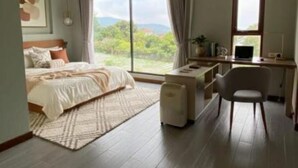 A bedroom with a bed, a desk, and a chair. There is a window with a view of greenery outside. - Shaionara Villa (Parongpong)