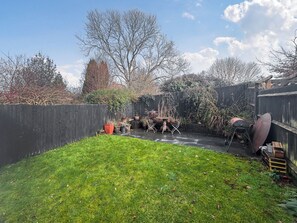 A backyard with a wooden fence, a barbecue grill, and a table with chairs.