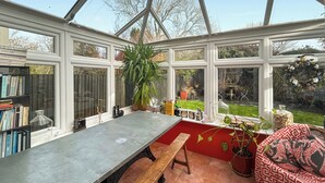 Ein Wintergarten mit Tisch, Bank und Blumentöpfen.