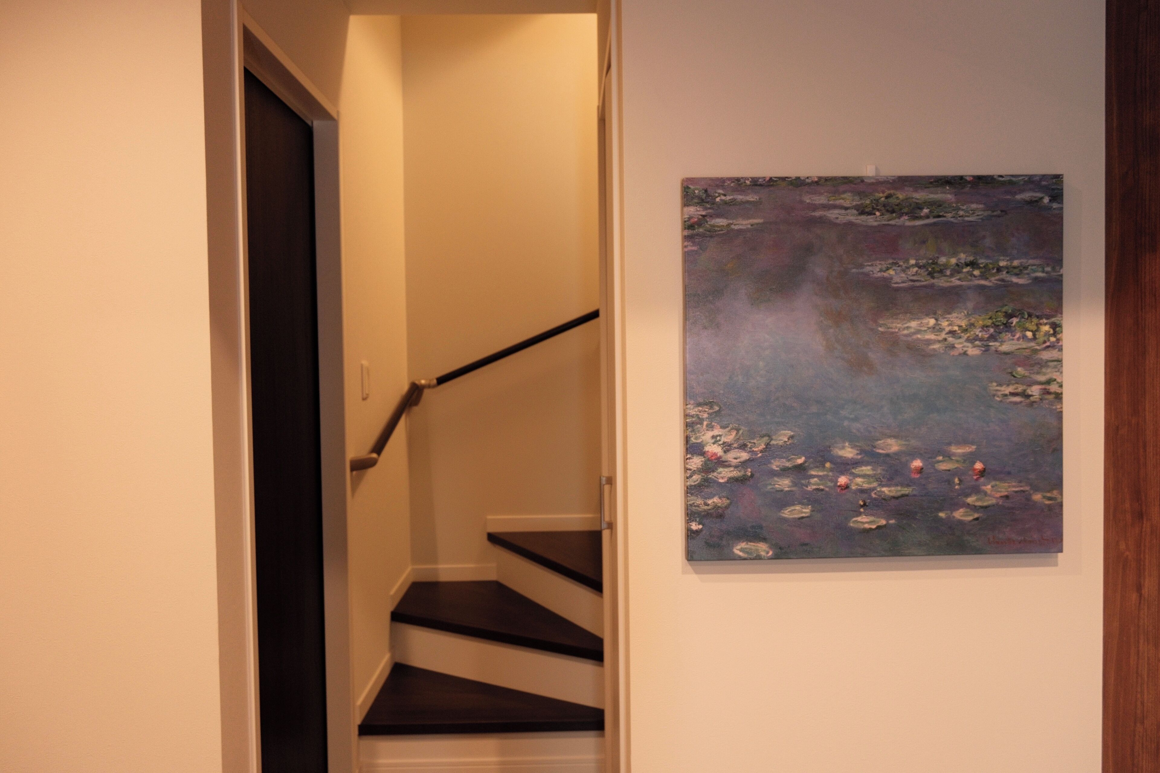 A staircase with a handrail leading to a landing, and a painting of water lilies on the adjacent wall.