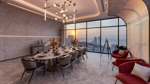 Ein moderner Essraum mit großem Tisch, gedeckt für sechs Personen, Stadtblick und einem roten Sofa.