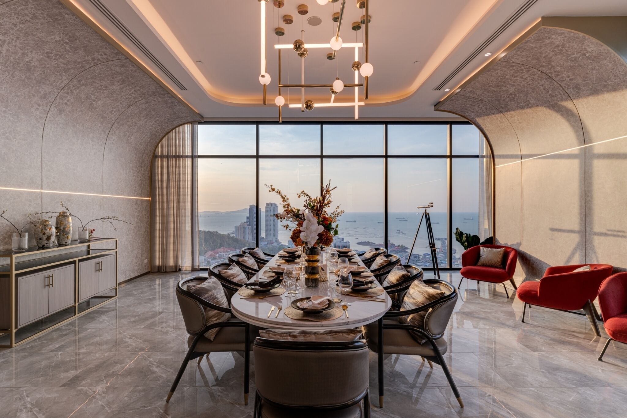 Une salle à manger moderne offrant une vue panoramique sur la ville, une table ronde dressée pour six personnes et un fauteuil rouge qui apporte une touche de couleur.