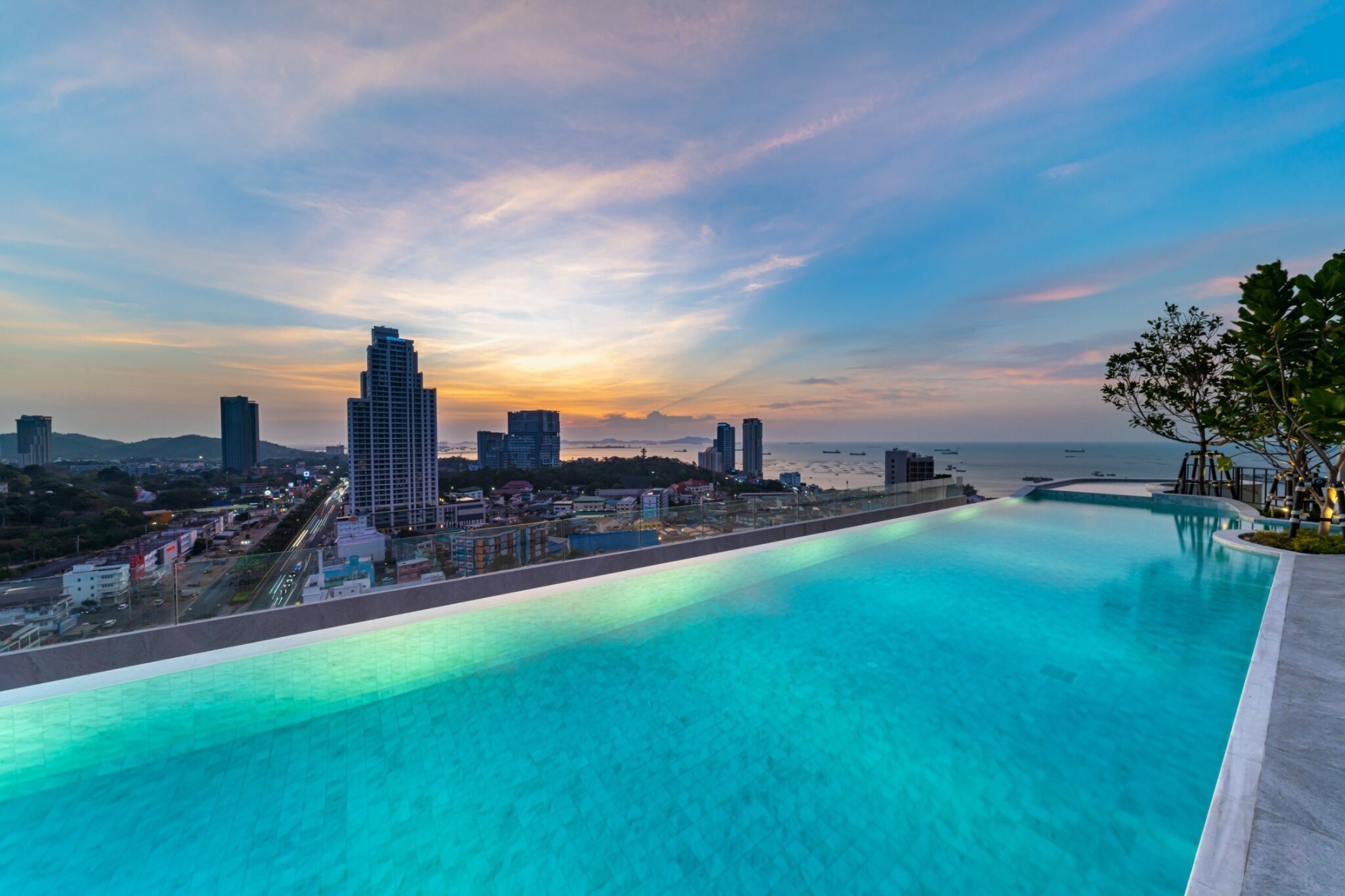 Paisagem urbana com uma piscina grande, edifícios modernos e um pôr do sol.