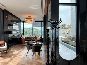 A modern hotel interior with a large window, a dining area, and a view of the surrounding landscape. - Hampton Sriracha (Si Racha)