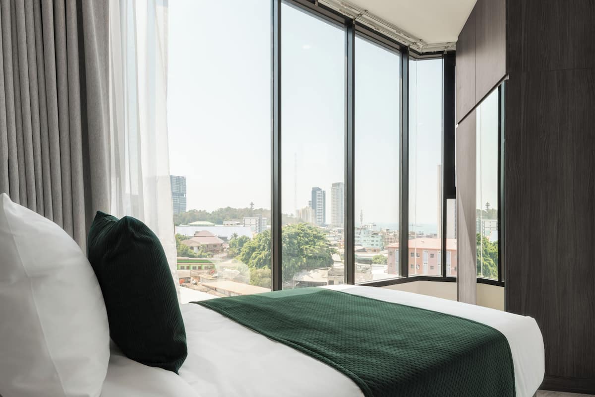 A hotel room with a large bed, a view of the cityscape through large windows, and a city view outside the window.
