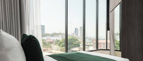 Un cuarto de hotel con una cama grande, vista del paisaje urbano a través de ventanas amplias y una vista de la ciudad desde la ventana.