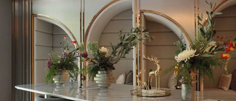 A modern bar area with a marble countertop, grey upholstered bar stools, and decorative floral arrangements.