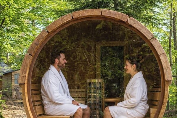 Two people in a wooden circular structure with benches, surrounded by greenery.