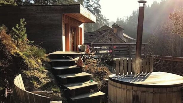 Eine Holzterrasse führt zu einem Whirlpool, im Hintergrund eine rustikale Holzhütte.