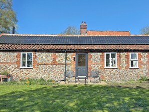 Una casa de piedra con techo de tejas, paneles solares y puerta principal.