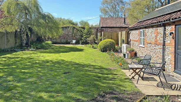 A garden with a lawn, a wooden bench, and a stone building with a tiled roof. - Sparrow Green Farm Cottage - UK50110 (Sparrow Green, near Dereham)
