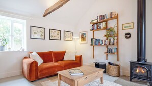 A cozy living room with a sofa, a coffee table, a bookshelf, a fireplace, and framed botanical prints on the wall. - Sparrow Green Farm Cottage - UK50110 (Sparrow Green, near Dereham)