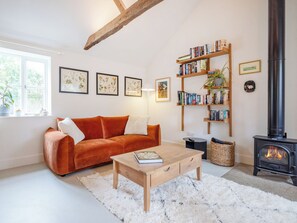 Una sala de estar acogedora con un sofá, una mesita de centro, una estantería, una chimenea e impresiones botánicas enmarcadas en la pared.