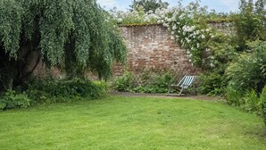 A grassy backyard with a brick wall, a tree, and a chair. - Sparrow Green Farm Cottage - UK50110 (Sparrow Green, near Dereham)