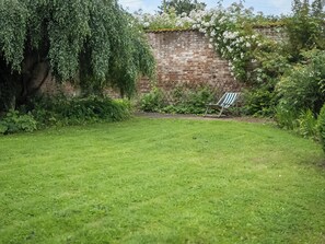 Patio cubierto de césped con un muro de ladrillo, un árbol y una silla.