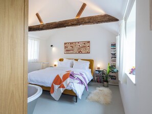 Un dormitorio con cama, radiador, estantería y ventana.