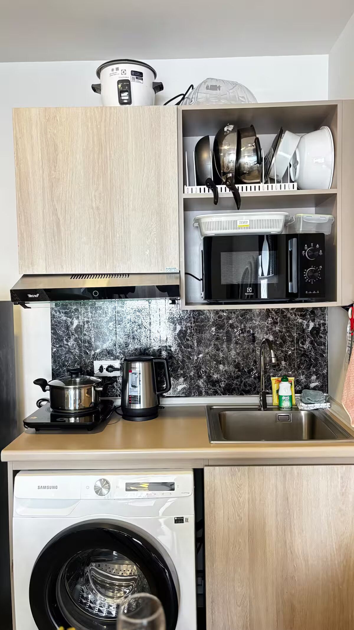 A compact kitchen with a microwave, stove, sink, and washing machine.