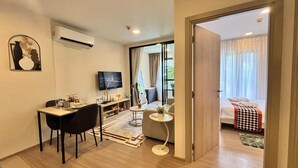 A modern hotel room with a dining area, a TV, a sofa, and a balcony with a bed. - 2 BR Dcondo Reef Phuket By Ploy (Kathu)