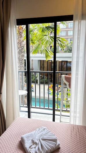 Een hotelkamer met een bed, een balkon met zwembad en uitzicht op palmbomen en gebouwen.