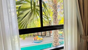 A room with a large window, white curtains, and a view of palm trees and a building outside. - 2 BR Dcondo Reef Phuket By Ploy (Kathu)