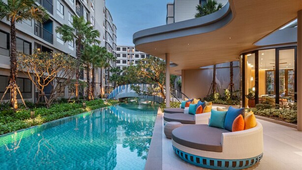 A modern hotel with a swimming pool, outdoor seating, and a bridge. - 2 BR Dcondo Reef Phuket By Ploy (Kathu)