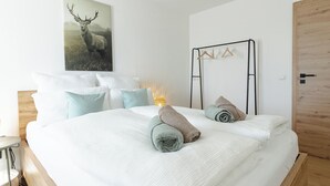 Une chambre à coucher avec un lit, des oreillers, une lampe fixée au mur, une porte en bois et un porte-manteau.
