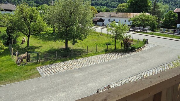 Une vue depuis un balcon donnant sur une route, avec une montagne en arrière-plan, une clôture et un bâtiment avec un toit rouge.