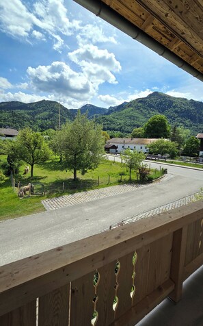 A view from a balcony overlooking a road with a mountain in the background, a fence, and a building with a red roof. - Simon Vacation Apartment, 90 m², sleeps 2–6, fully equipped kitchen, 3 bedrooms, shower/toilet + separate toilet, balcony (Staudach-Egerndach)
