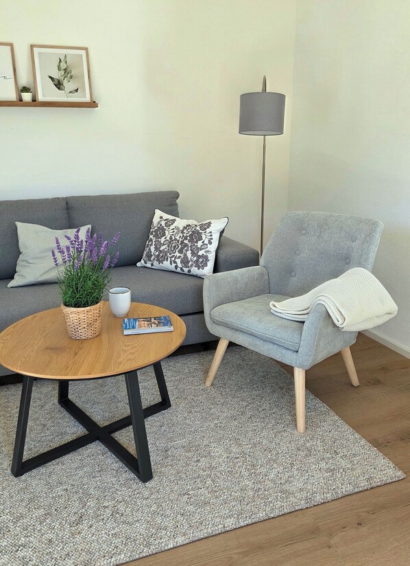 Un salon avec un canapé gris, une table basse ronde, un fauteuil gris, un lampadaire et une petite plante en pot.