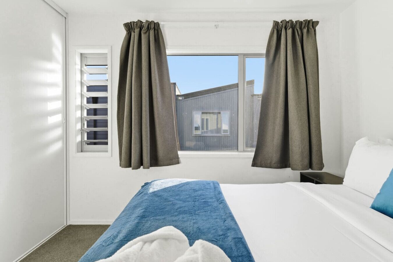 A hotel room with a bed, a window with blinds, and curtains.