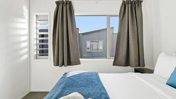 A hotel room with a bed, a window with blinds, and curtains.