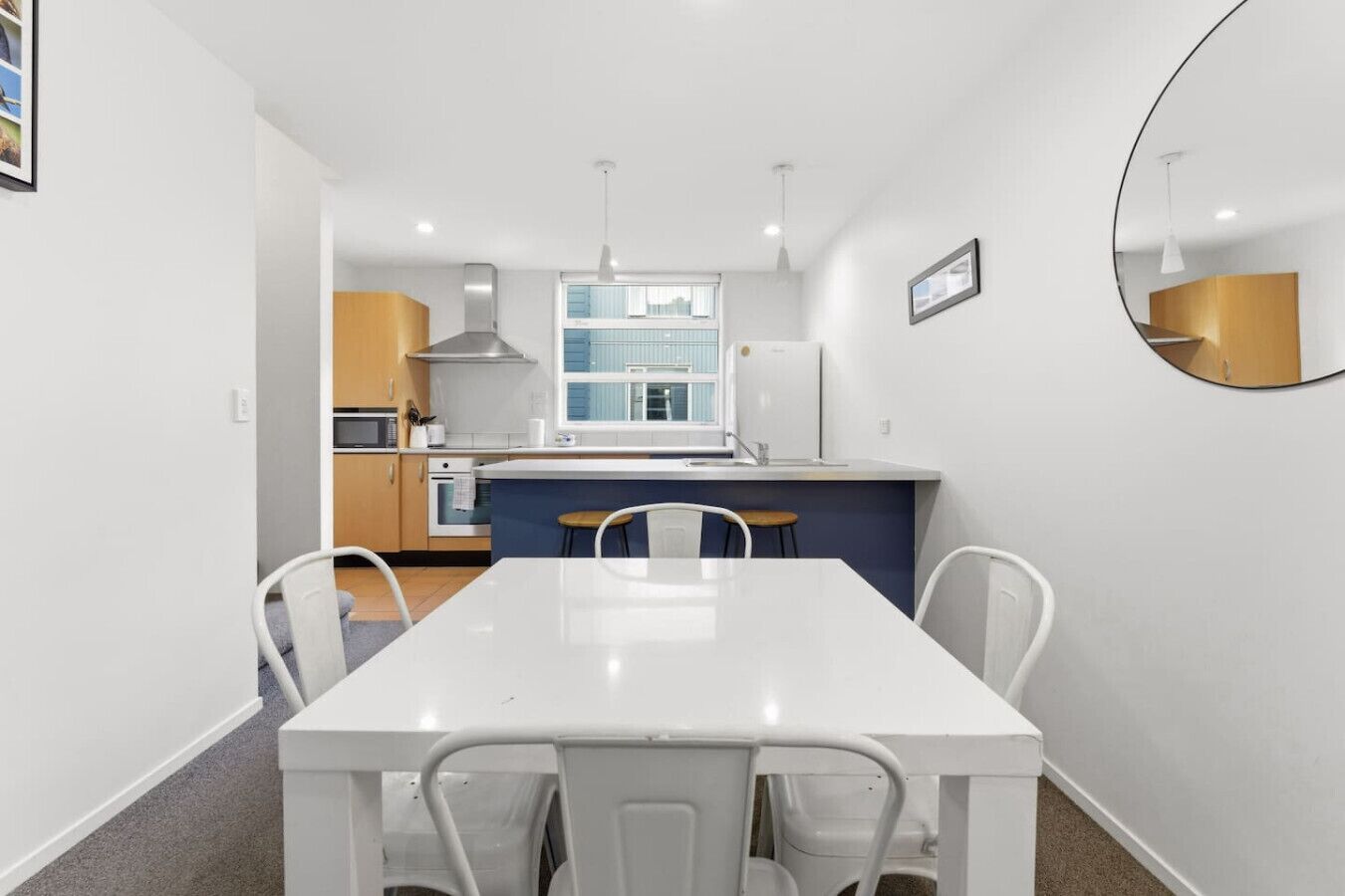 A modern kitchen with white cabinets, a central island, and a dining area with a white table and chairs.