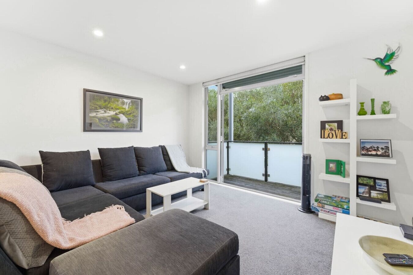 A modern living room with a grey sofa, a white coffee table, and a large window with a view of greenery.