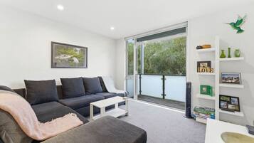 A modern living room with a grey sofa, a white coffee table, and a large window with a view of greenery.