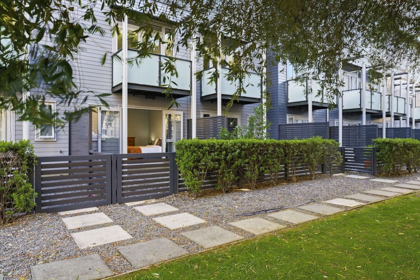 A modern residential building with a covered outdoor seating area, a gated entrance, and a well-maintained garden.