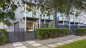Ein modernes Wohngebäude mit überdachter Außenbestuhlung, einem verschlossenen Eingangsbereich und einem gepflegten Garten.