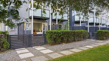 A modern residential building with a covered outdoor seating area, a gated entrance, and a well-maintained garden.