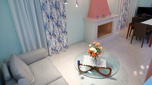 A living room with a sofa, a glass coffee table with a vase of flowers, a fireplace, and a dining area with chairs. - Villa Eudora Nafpaktos (Nafpaktos)