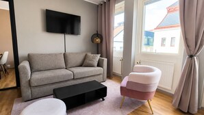 Ett modernt vardagsrum med en grå soffa, ett svart soffbord, en rosa fåtölj och en tv som är monterad på väggen.