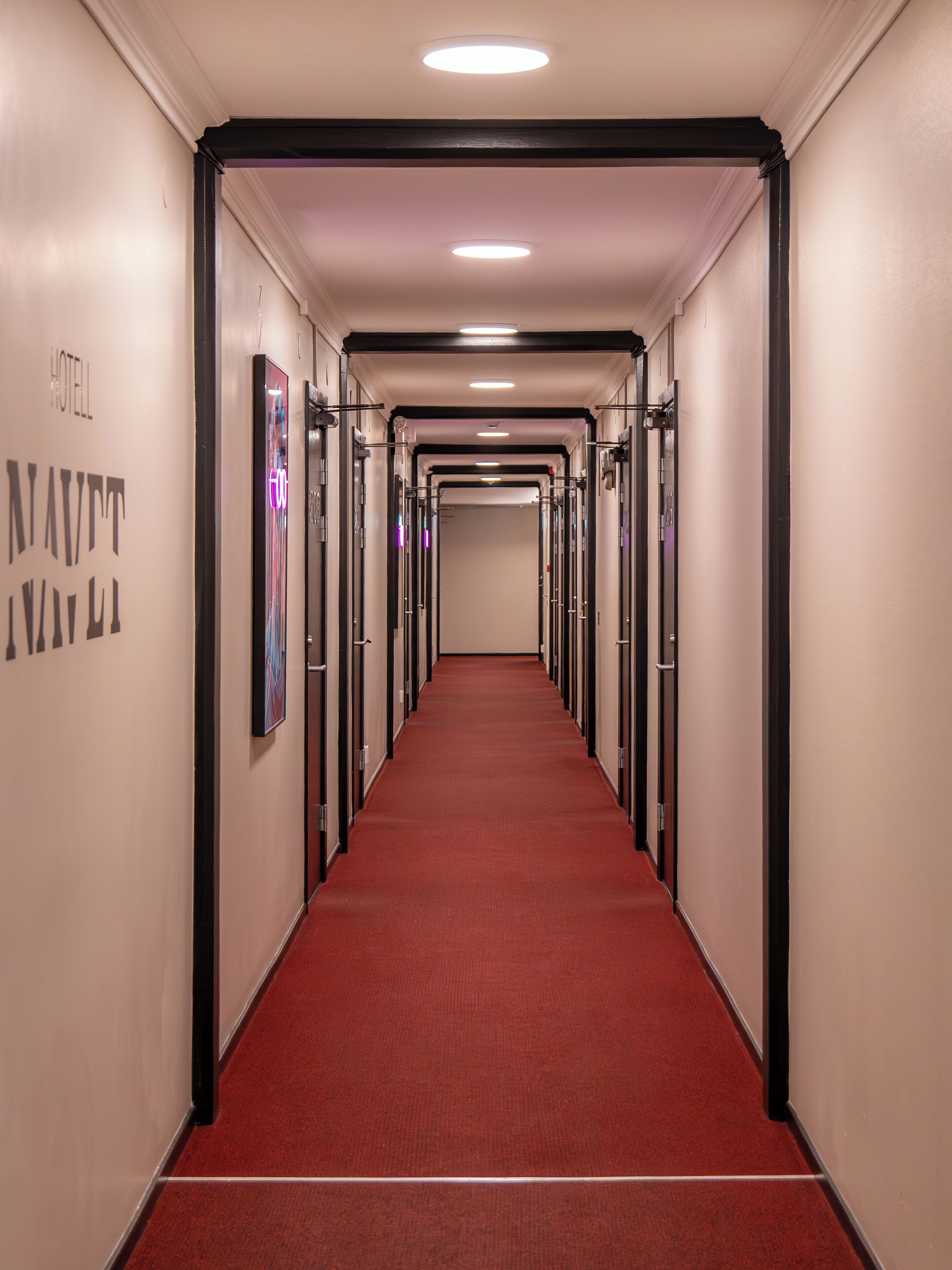 Un couloir d’hôtel avec un tapis rouge, de nombreuses portes et un plafond doté d’un éclairage encastré.