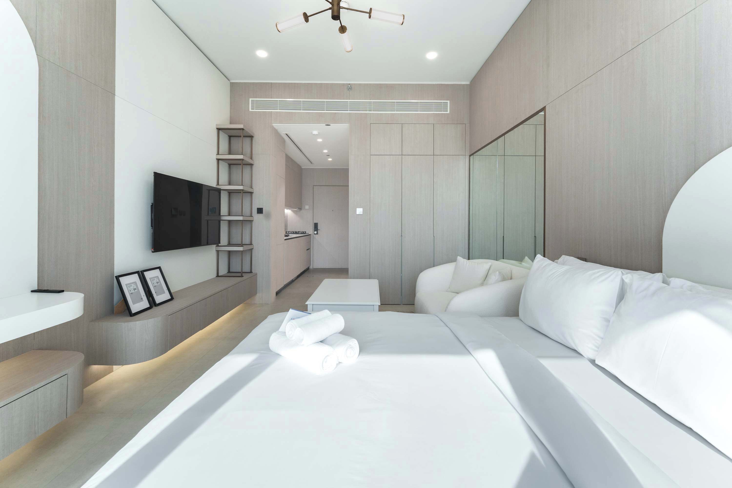 Una habitación de hotel moderna con una cama grande, un televisor de pantalla plana montado en la pared, un estante empotrado y un espejo.