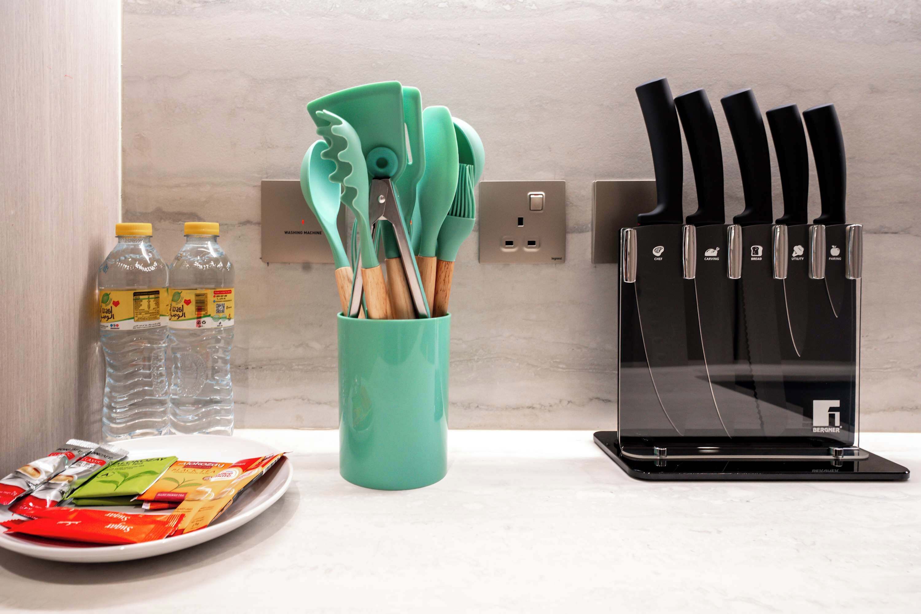 Un plan de travail de cuisine avec un range-couteaux, un porte-ustensiles vert et des bouteilles d’eau.
