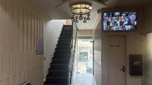A hotel hallway with a staircase, a chandelier, a multi-camera security system, and a sign for the wash room. - Hotel Rajshree (Hisar)