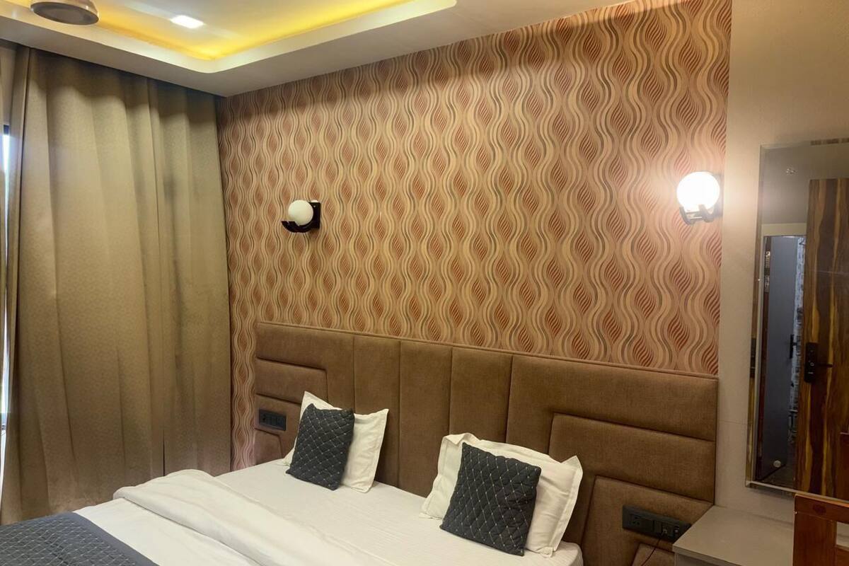 A hotel room with a large bed, a headboard, a wall-mounted light, and a window with curtains.