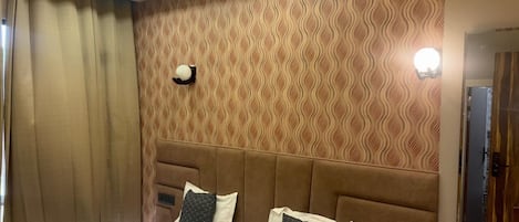 A hotel room with a large bed, a headboard, a wall-mounted light, and a window with curtains.